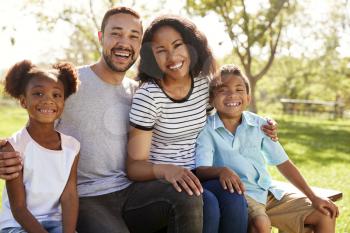 Outdoor Portrait Of Smiling Family Sitting On Bench In Park