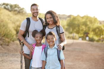 Portrait Of Family Wearing Backpacks Hiking In Countryside Together