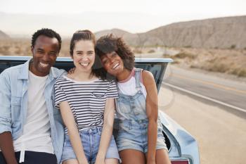 Portrait Of Three Friends Sitting In Trunk Of Classic Car On Road Trip