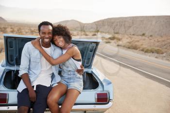 Portrait Of Couple Sitting In Trunk Of Classic Car On Road Trip