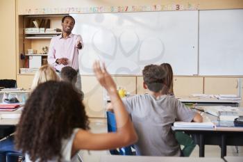 Teacher pointing to girl with hand raised in school class
