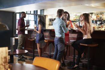 Group Of Young Friends Relaxing In Bar Standing At Counter