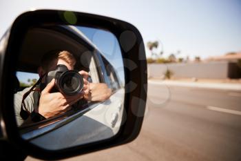 Young man in car taking photo, seen in wing mirror