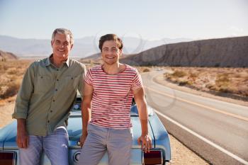 Father and adult son on road trip leaning against their car