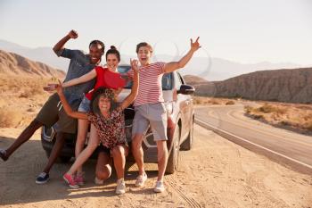 Young adult friends on road trip have fun posing by the car