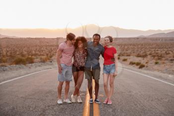 Four friends standing on a desert highway looking to camera