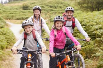 Portrait of parents and children sitting on mountain bikes in a country lane during a family camping trip, front view