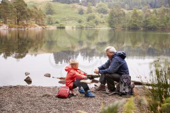 Grandfather and grandson sitting at the shore of a lake talking, elevated view, Lake District, UK