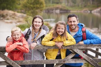 Young family leaning on a wooden fence in the countryside, looking at camera, close up