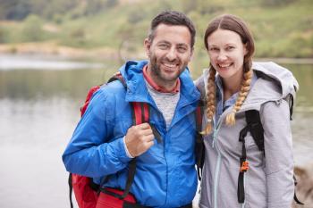 Young adult couple on a camping trip standing near a lake looking to camera, close up, Lake District, UK