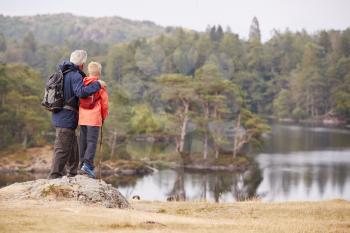 Grandfather and grandson standing on a rock admiring the view of a lake, back view, Lake District, UK