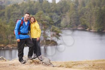 Caucasian pre-teen girl standing with her father on a rock by a lake, smiling to camera, lakeside background