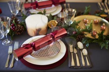 Close up of Christmas table setting with crackers arranged on plates and red and green table decorations, close up