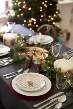 Christmas table setting with bauble name card holder arranged on a plate and green and red table decorations, Christmas tree in the background, elevated view