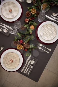 Christmas table setting with baubles arranged on plates and green and red table decorations, overhead view, vertical