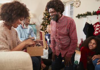 Couple Exchanging Gifts As Multi Generation Family Celebrate Christmas At Home Together