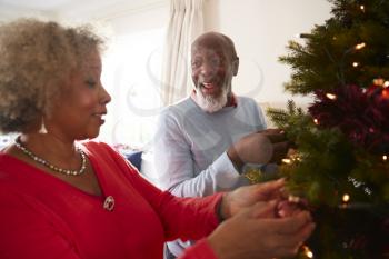 Senior Couple Hanging Decorations On Christmas Tree At Home Together