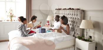 Young mixed race family sitting on bed opening gifts in parents bedroom on Christmas morning