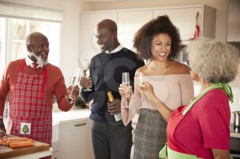 Mixed race senior and young adult family raise champagne glasses to celebrate, while preparing Christmas dinner together in the kitchen, close up