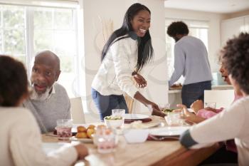 Black couple bringing food to the table for Sunday family dinner for the kids and grandparents