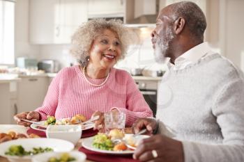 Senior black couple smiling to each other as they eat Sunday dinner together at home, close up