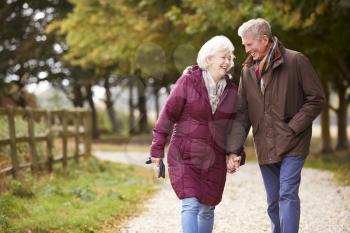 Active Senior Couple On Autumn Walk On Path Through Countryside