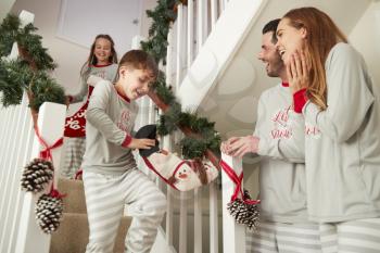 Parents Greeting Excited Children Wearing Pajamas Running Down Stairs Holding Stockings On Christmas Morning