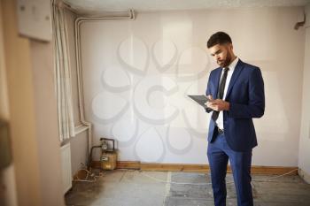 Male Realtor With Digital Tablet Carrying Out Valuation On Property For Renovation