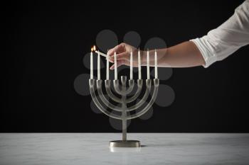 Hand Lighting Candle On Metal Hanukkah Menorah On Marble Surface Against Black Studio Background