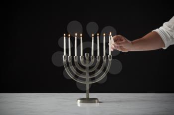 Hand Lighting Candle On Metal Hanukkah Menorah On Marble Surface Against Black Studio Background