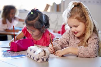 Two young schoolgirls sitting at a desk in an infant school classroom working, close up