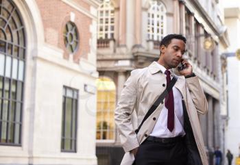 Millennial black businessman standing on a street in London talking on his phone, low angle