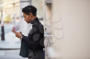 Young black woman standing on a street in London using her smartphone, side view, close up, selective focus