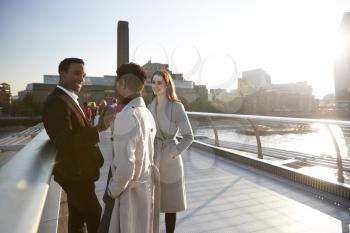 Three millennial colleagues stand talking on Millennium Bridge as the sun goes down