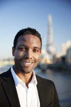Young black businessman in smart casual clothing standing by the River Thames in London smiling to camera, close up