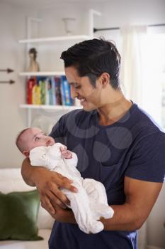 Proud Hispanic father holding his four month old child at home, waist up, vertical