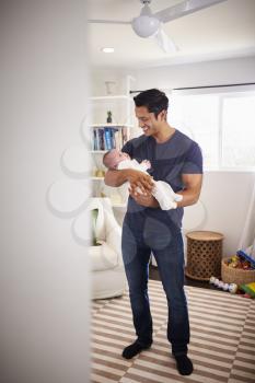 Proud Hispanic father holding his four month old child at home, seen from doorway, vertical