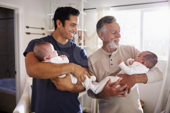 Young Hispanic man and his senior father holding his two baby boys at home