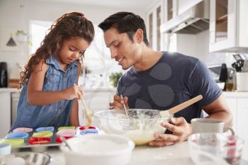 Young girl standing at the kitchen table making cakes with her father, filling cake forms, close up