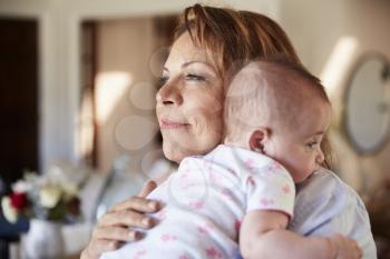 Middle aged Hispanic grandmother holding her newborn grandson, head and shoulders, close up