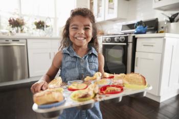 Young Hispanic girl standing in kitchen presenting cakes shes baked and smiling to camera