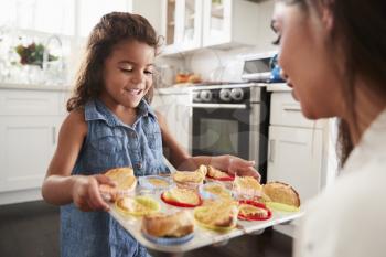 Smiling young Hispanic girl standing in kitchen presenting the cakes she has baked to her mother