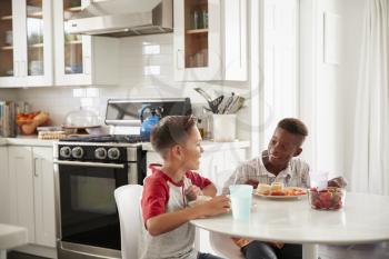 Two pre-teen male friends sit talking in the kitchen during a playdate at one boys house