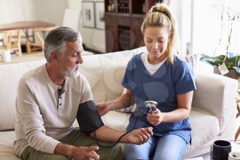 Female healthcare worker making home visit to a senior man taking blood pressure