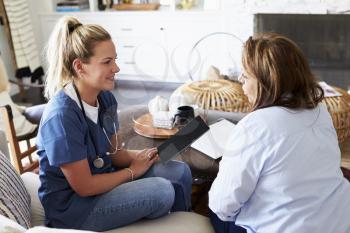 Female healthcare worker sitting on the sofa with a middle aged woman during a home health visit
