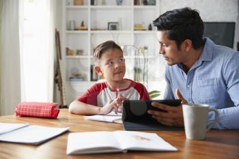 Hispanic pre-teen boy sitting at dining room table working with his home school tutor