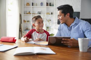 Hispanic pre-teen boy sitting at table working with his home school tutor, smiling at each other