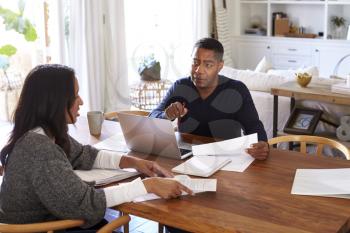 Millennial man with laptop computer giving financial advice to a woman sitting at the table holding a document in her dining room, side view
