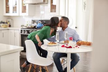 Middle aged mixed race woman woman kissing her partner after serving him a romantic meal in their kitchen, selective focus