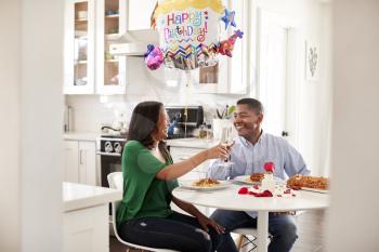 Middle aged mixed race couple making a toast over a romantic birthday meal in their kitchen, close up